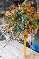 Man holding finished rustic orange, green and blue festive wreath in workshop