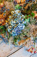 close up detail of festive wreath on workbench with dried hydrangea flowerhead and allium seedhead