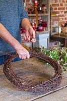 Man building up layers of birch branches to make rustic wreath form. 