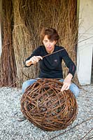 Woman making ornamental sphere out of woven willow stems.
