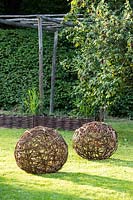 Woven willow spheres displayed on lawn in garden.