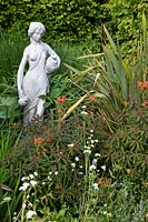 Female figure in border with Euphorbia griffithii and other perennials 