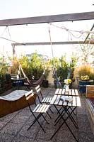 Seating area and hammocks are surrounded by potted plants on roof garden of hostel.