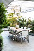 Covered dining area on terrace screened by container grown shrubs 