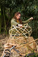 Woman in commercial bamboo clearing, hand weaving strips of different sizes of bamboo to create a lampshade