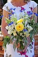 Woman with bouquet of early-summer flowers, including yellow roses. cornflowers and chamomile.