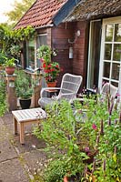 Relaxing area on small patio, paving slabs near house with chairs, table and container plants such as Agastache rugosa and Salvia in pots