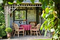 Outdoor relaxing area, table and chairs inside open-fronted summerhouse with window and trellis top 