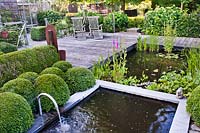 Relaxing area on decked patio by a ponds, upper pond formal with water spout and Buxus - Box - ball topiary and lower pond with marginal and aquatic plants