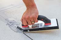 Man using a grout float to fill context Porcelain patio with porcelain grout