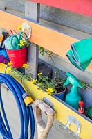 Close up detail of rainbow coloured pallet organiser, holding various garden tools, attached to shed wall 