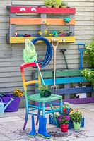 Rainbow coloured pallet tool organiser attached to an outside wall of a shed with matching chair 