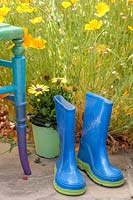 Blue welly boats on patio with colourful chair and potted Osteospermum