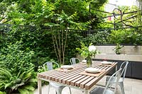 A dining area and outdoor kitchen, screened by metal fencing and foliage planting of trees, shrubs and climbers 