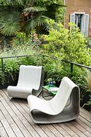 Corner of decked terrace with metal rail, privacy from neighbouring building provided by Nerium oleander and Trachycarpus fortune - Palm, in the foreground planters of Stipa tenuissima, Miscanthus 'Morning Light', Agapanthus 'Blue Storm' and Pittosporum heterophyllum provide a screen for relaxed seating 