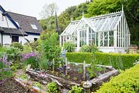 Kitchen garden enclosed by low hedging with traditional greenhouse and house in background