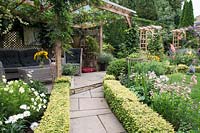 Path leading to a dining area under wooden pergola in cottage garden 