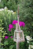 Garden candle lantern hung from a post, in front of a mixed border 