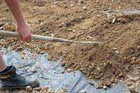 Man using a rake to level out sand, hardcore and gravel mix ontop of membrane
