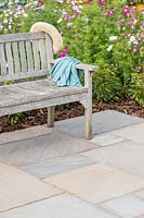 Patio laid with riven sandstone paving in 'Country Green' colour scheme with wooden bench