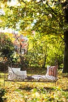 Rustic day bed with cushions on lawn with fallen leaves