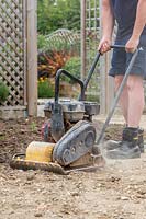 Man using wacker plate to compact base for laying patio