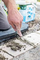 Man using pointing trowel to fill paving joints with pointing material