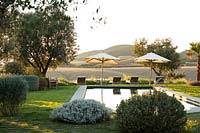 Swimming pool set in grass with low shrubs, sun loungers look out over fields and countryside landscape