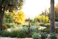 A dry garden of evergreen shrubs and trees with weathered steel Opuntia sculpture