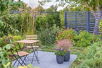 Small patio with bistro table and chairs in tiny garden with mixed planting and wooden fencing 