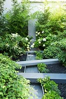 Mixed planting surrounding a metal water feature including hydrangea paniculata 'levana', ferns