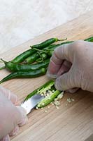 Person scraping out the seeds of green cayenne chilli with an antique serrated knife.