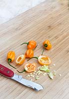 Whole and cut open orange Habanero Chillies with scraped out seeds and pith on a timber chopping board.