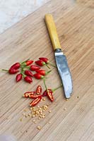 Whole and cut open Birds Eye Chillies with scraped out seeds and pith on a timber chopping board.