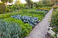Vegetable garden with a paved path: leeks, carrots, cabbages, chards, marigolds, pumpkins and kale.
