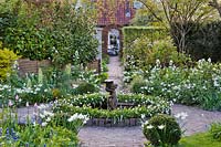 White themed planting in spring featuring daffodils, Anemone blands, tulips, Fritillaria persica 'Ivory Bells' and Lunaria annua. Small central circular pond with statue.
