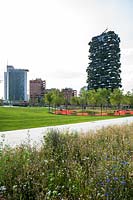 View across wildflower planting to public park with circle of trees, in background city scape including Bosco Verticale - Vertical Forest - designed by Stefano Boeri 