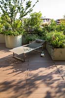 View over decked terrace to sun lounger with containers providing a screen from edge. Round container with Acer palmatum 'Crispifolium', other trough planters with foliage perennials.