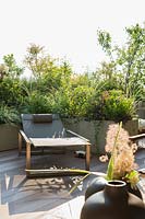 Sun lounger on decked terrace with bank of containers of mixed foliage providing a screen