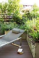 L-shaped layout of trough planters, filled with mixed foliage, on decked terrace provide a relaxing corner