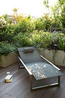 Sun lounger on decked terrace with a living screen of shrub and perennial foliage in trough planters 