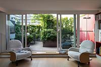 View from insider through sliding glass doors to roof garden, on one side a with pergola with climbers, on the other planters with shrubs and a red partition 