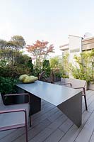 On decked roof garden looking back to building, table and chairs with plant screen of trees and shrubs