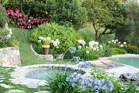 View over the swimming pool with stone edge and nearby flower beds with Agapanthus and the outdoor 