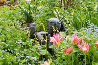 Sculpture surrounded by Tulipa 'Virichic' - viridiflora tulip, Brunnera macrophylla and Tellima grandiflora.