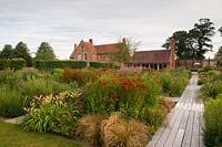 View along decked path next to large flowerbeds in modern formal country garden 