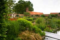 Modern formal country garden, view over deep flower beds with decked path to walls and buildings 