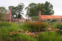 Modern country garden, view over flower beds to buildings and trees