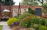 Corten steel pergola above seating area against brick wall of a walled country garden, in foreground corner of a perennial flower bed 