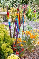 Ribbons in the colour of the rainbow tied to hazel poles in a flower bed 